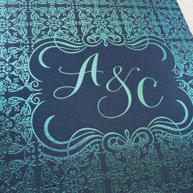 Close-up of teal foil stamped Italian tile pattern on the back of a luxury Italy wedding invitation with custom monogram.
